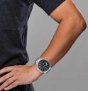 Man draagt een Seiko chronograaf horloge met blauwe wijzerplaat, zilverkleurige kast en band om de pols.