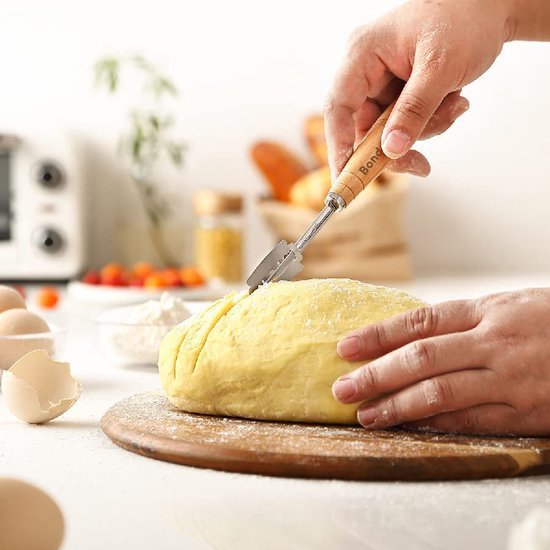Handen maken inkepingen in een geel brooddeeg met een deegmes, op een ronde houten plank.