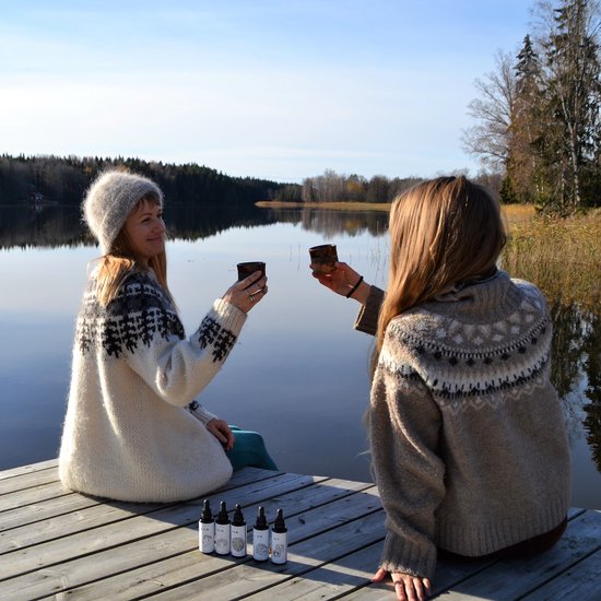 Twee vrouwen in gebreide truien met fair isle-patroon toasten met mokken op een houten pier aan een meer.