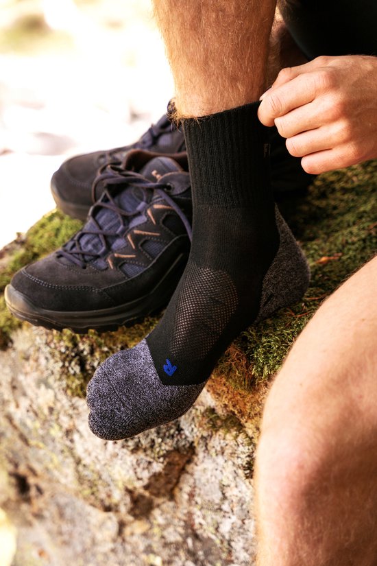 Un homme enfile une chaussette de randonnée Falke gris foncé près de chaussures de randonnée, gros plan.