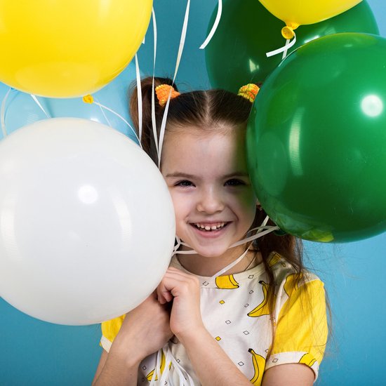 Lachend meisje met banaanprint shirt, te midden van gele, groene en witte ballonnen.