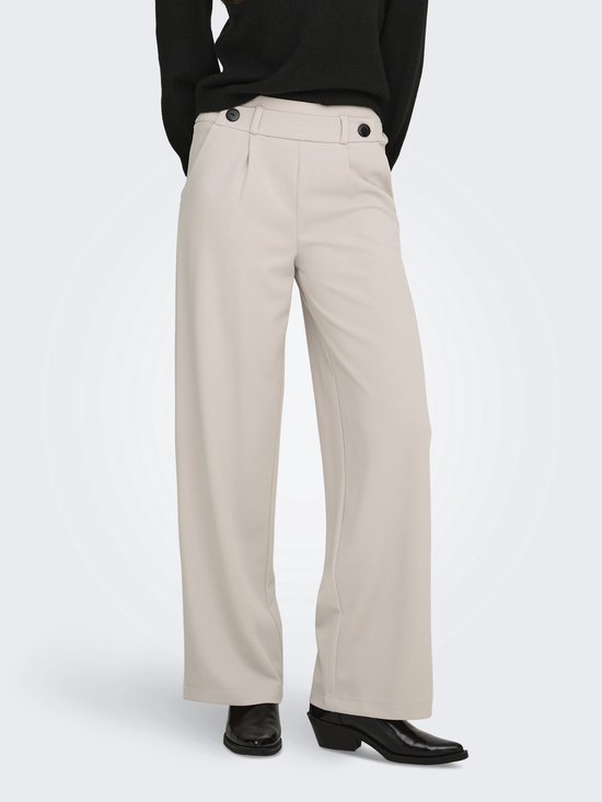 Model met beige wijde broek met knopen en zwarte coltrui, zicht op de voorkant.