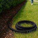 Zwarte tuinslang liggend op gras en aarde, met een groen koppelstuk aan het einde.