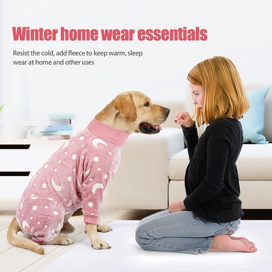 Meisje knielt bij hond in roze pyjama met maan- en sterrenprint. 'Winter home wear essentials'.