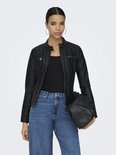 Vrouw met hoge paardenstaart in een zwarte faux leren bikerjack met ritsen, jeans en tas.