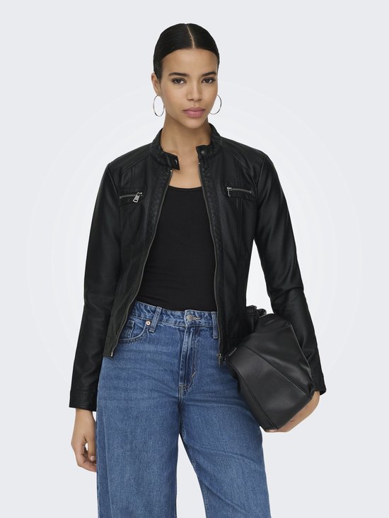 Vrouw met hoge paardenstaart in een zwarte faux leren bikerjack met ritsen, jeans en tas.