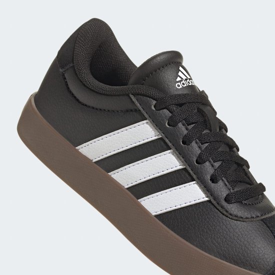 Close-up van zwarte adidas sneaker met witte strepen en bruine zool.