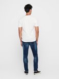 Man in skinny jeans met donkere wassing, wit t-shirt en zwarte sneakers, van achteren gezien.