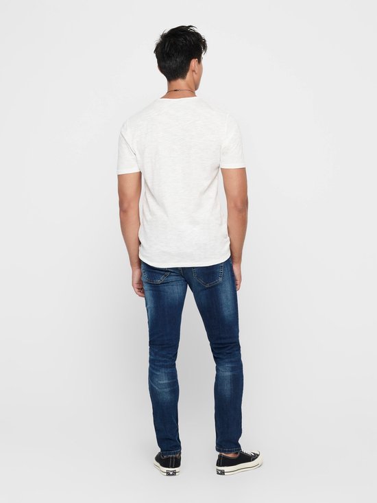 Man in skinny jeans met donkere wassing, wit t-shirt en zwarte sneakers, van achteren gezien.