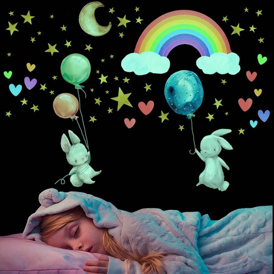 Une fille dort entourée de stickers muraux lumineux représentant des lapins avec des ballons, un arc-en-ciel, une lune et des étoiles.
