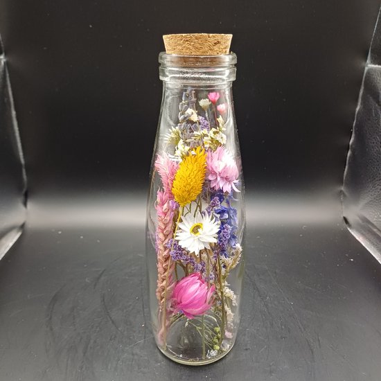 Glazen fles met een kurk, gevuld met gedroogde bloemen in roze, paars, geel en wit.