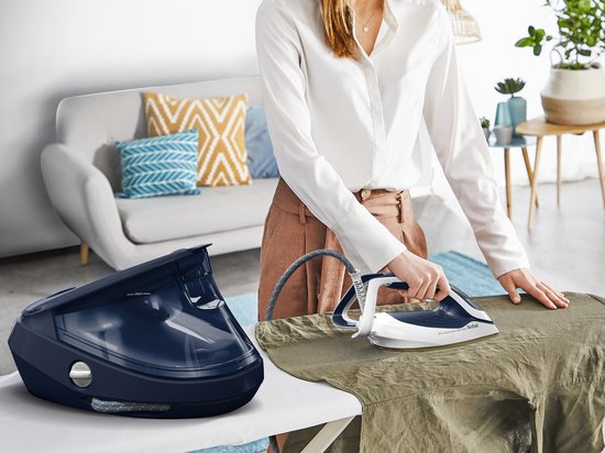 Een vrouw strijkt een groen overhemd met de Tefal Pro Express Ultimate II. Naast de strijkplank staat een donkerblauwe stoomgenerator.