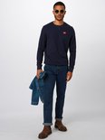 Man met zonnebril in donkerblauwe Wrangler jeans, marineblauwe trui met rood logo, bruine laarzen.