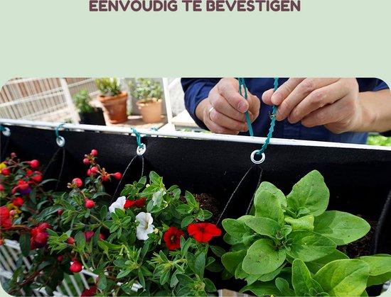 Handen bevestigen een zwarte verticale plantenbak gevuld met bloeiende rode en witte bloemen, groene planten en rode bessen.