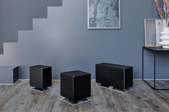Drie zwarte luchtbevochtigers op een houten vloer bij een trap.