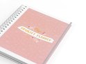 Close-up van een koraalkleurige ringband-planner met gouden tekst 'Myn Bruiloft Planner'.