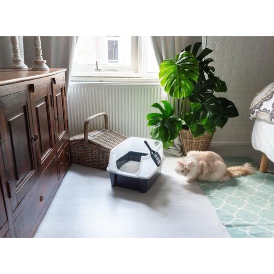Donkergrijze kattenbak met witte kap staat op een lichtgrijze vloer, naast een mand. Een kat ligt naast de bak.