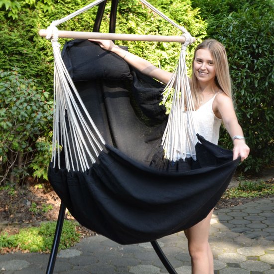 Vrolijke vrouw met blond haar laat de zwarte hangmatstof van een hangstoel zien, buiten.