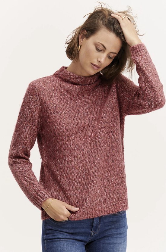 Model draagt een roze gebreide trui met een hoge hals en gemêleerde textuur, met de hand in het haar.