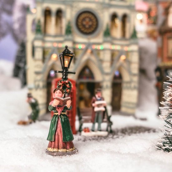 Vrouw met boek voor een kerk en telefooncel in een besneeuwd dorp.