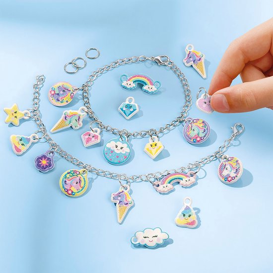 Kinderhandje pakt een roze hartvormige bedel, met twee zilveren bedelarmbanden en losse bedels.