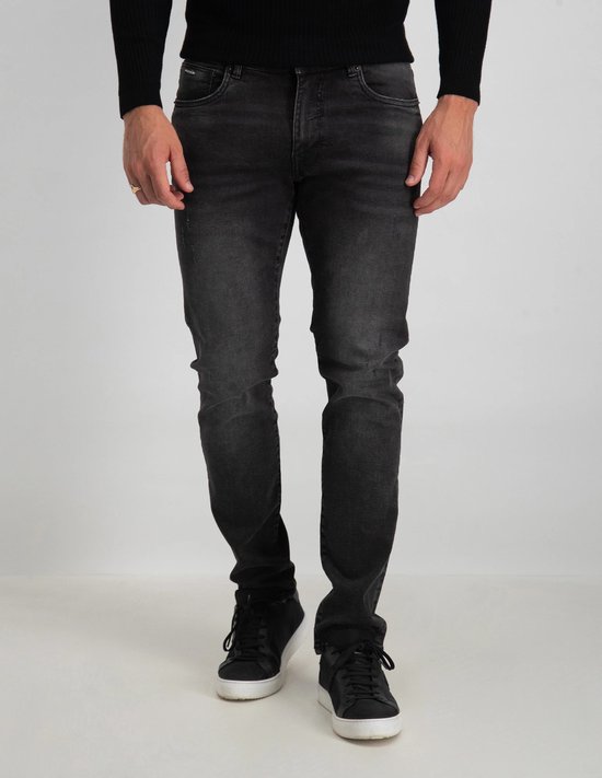 Man in een zwarte trui en donkergrijze slim fit jeans met lichte slijtage en sneakers.