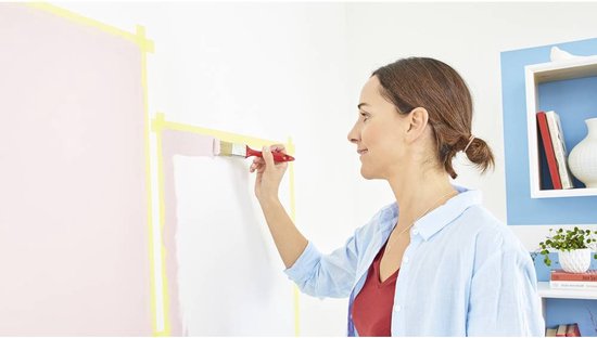 Vrouw schildert met een kwast langs gele tape op een muur.