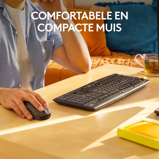 Man gebruikt een zwarte Logitech draadloze muis en toetsenbord op een bureau. Tekst 'COMFORTABELE EN COMPACTE MUIS'.