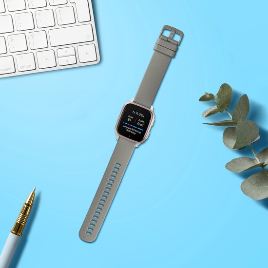 Bracelet de montre connectée gris avec boîtier doré rose, posé sur un bureau bleu.