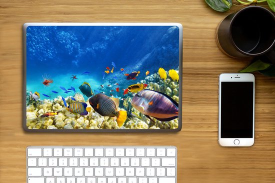 Ordinateur portable avec autocollant monde sous-marin : coraux, poissons et poisson-lion, sur un bureau avec clavier et téléphone.