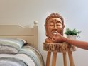 Gouden Boeddha hoofd met witte tissue uit de mond, op een houten bijzettafel naast een bed.