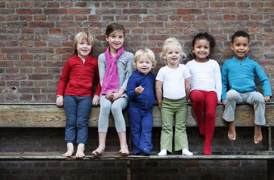 Zes lachende kinderen, jongen en meisjes, zittend op een bank. Variërend in kleding en haarkleur.