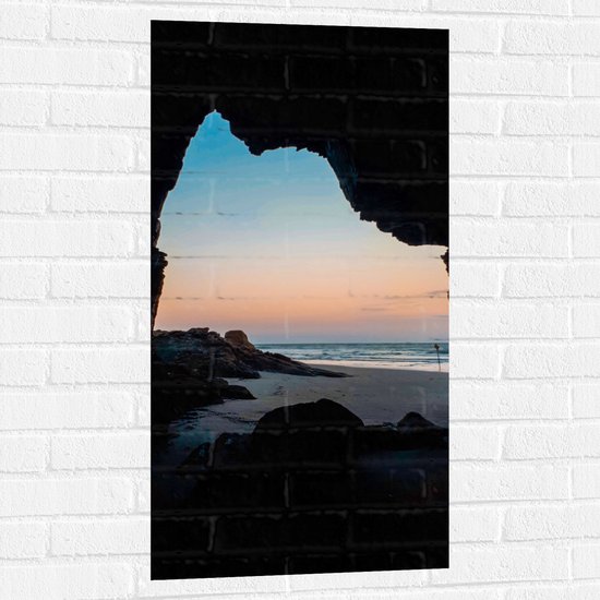 WallClassics - Muursticker - Ondergaande Zon aan Strand onder Rots - 50x100 cm Foto op Muursticker