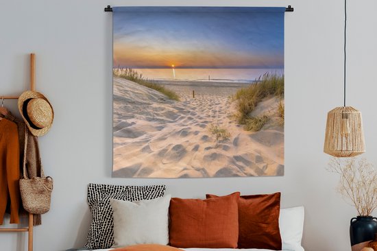 Wandkleed met duinlandschap en zonsondergang boven een rustige zee, hangend boven een bed met kussens.