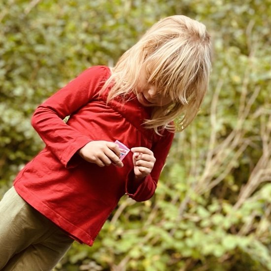 Meisje met blond haar in een rood wikkelvestje en lichtgroene broek, kijkt naar een klein pakje.