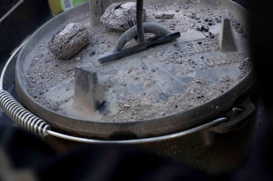 Zwarte metalen deksellifter met spiraalhandvat in een stoffig Dutch oven.