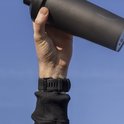 Persoon met een zwarte smartwatch met rubberen band houdt een zwarte shaker omhoog.
