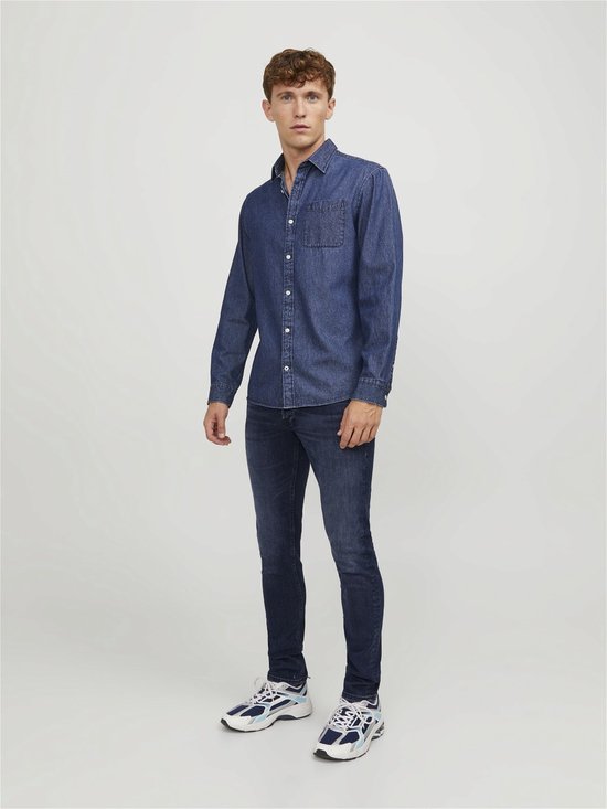 Man in een donkerblauwe denim jeans en een bijpassend spijkerhemd.