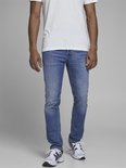 Man in een witte t-shirt en lichtblauwe skinny jeans met witte sneakers.