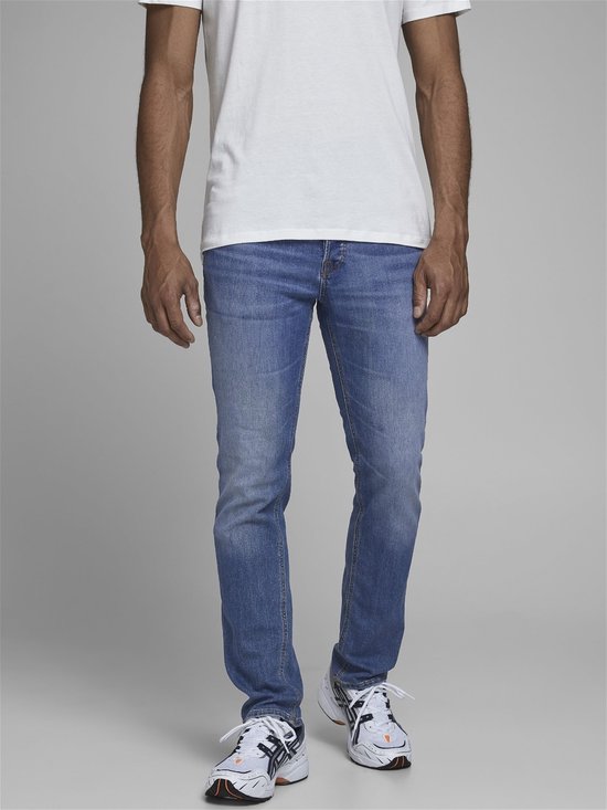 Man in een witte t-shirt en lichtblauwe skinny jeans met witte sneakers.