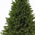 Detail van een volle, groene kunstkerstboom tegen een witte achtergrond.