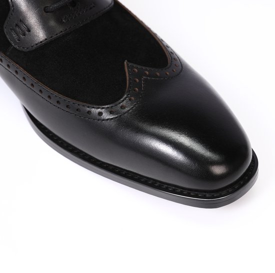 Neus van een zwarte leren veterschoen met suède en wingtip details.