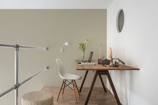 Werkruimte met bureau, laptop, stoel, plant en een opgestoffeerde poef.