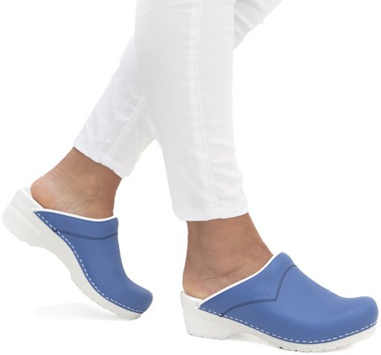 Blauwe Sanita klompen gedragen aan voeten met een witte broek.