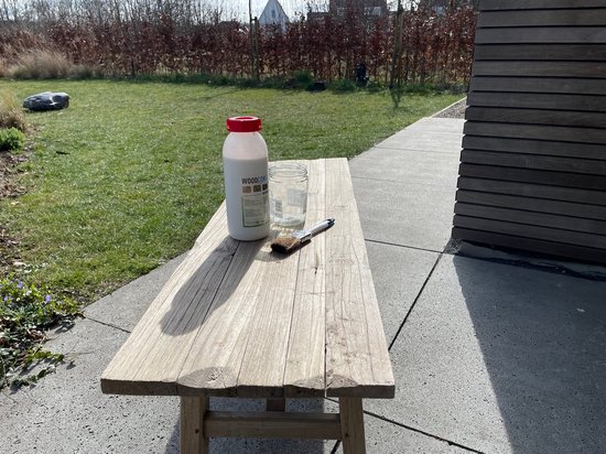 Fles Woodcon en glas met water op een houten bank in de tuin.