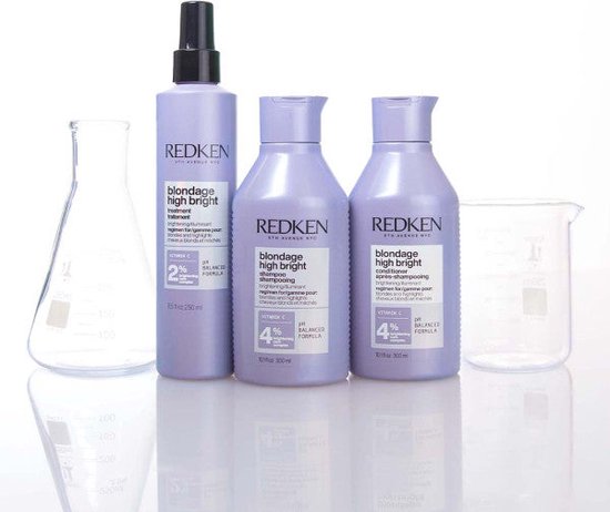 Trois bouteilles Redken avec de la verrerie de laboratoire. Shampooing, après-shampooing et pré-traitement dans des emballages violet clair.