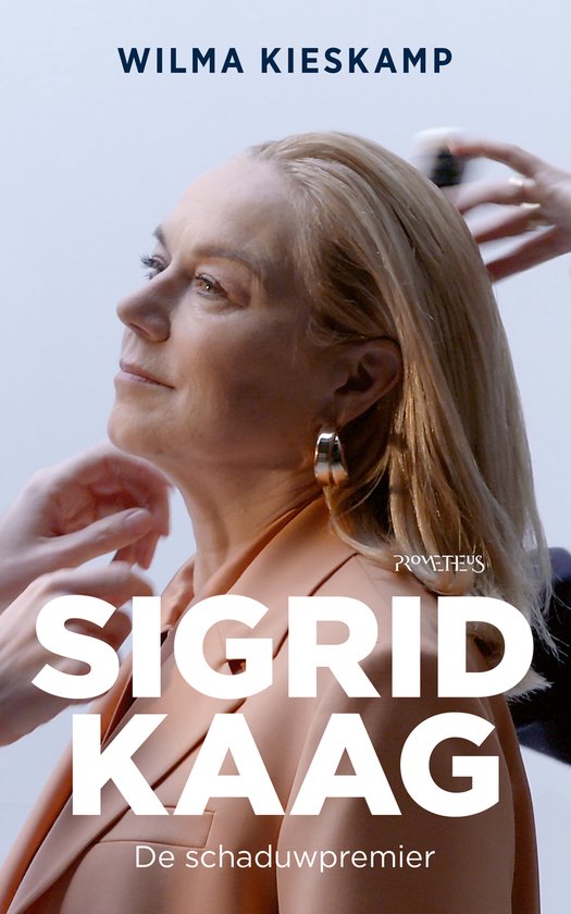 Vrouw met blond haar, naar links kijkend, met een oranje blouse en gouden oorbellen. Tekst: SIGRID KAAG De schaduwpremier.