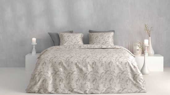Een tweepersoonsbed opgemaakt met een lichtbeige dekbedovertrek met een grijs gebladerte patroon. Twee grijze kussens liggen achter twee bijpassende kussenslopen.