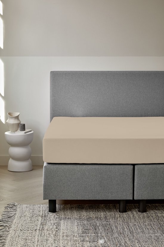 Drap-housse naturel sur un lit avec tête de lit grise.