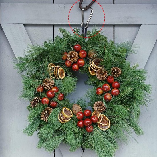 Kerstkrans met dennentakken, dennenappels, rode besjes en gedroogde sinaasappelschijfjes, opgehangen aan een karabijnhaak.